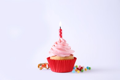 Photo of Delicious birthday cupcake with burning candle, sprinkles and streamer on white background