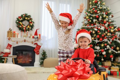 Photo of Cute little children playing with toy car in room decorated for Christmas