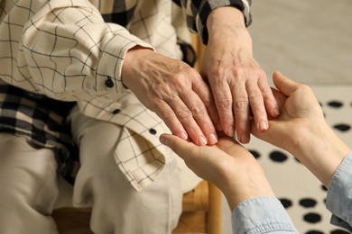 Photo of Young and elderly women holding hands indoors, closeup