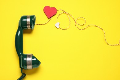Photo of Long-distance relationship concept. Telephone receiver, decorative cord and paper heart on yellow background, flat lay with space for text