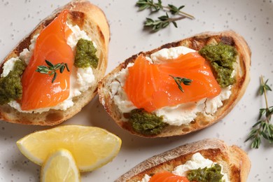 Photo of Delicious bruschettas with cream cheese, salmon and pesto sauce on plate, top view