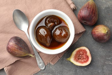 Photo of Bowl of tasty sweet jam, fresh figs and spoon on grey table, flat lay