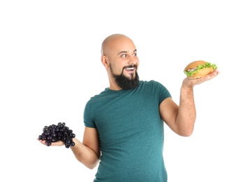 Photo of Overweight man with hamburger and grapes on white background