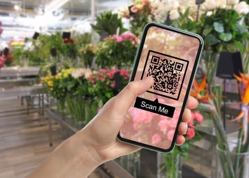 Image of Woman holding smartphone with QR code on screen in flower shop, closeup