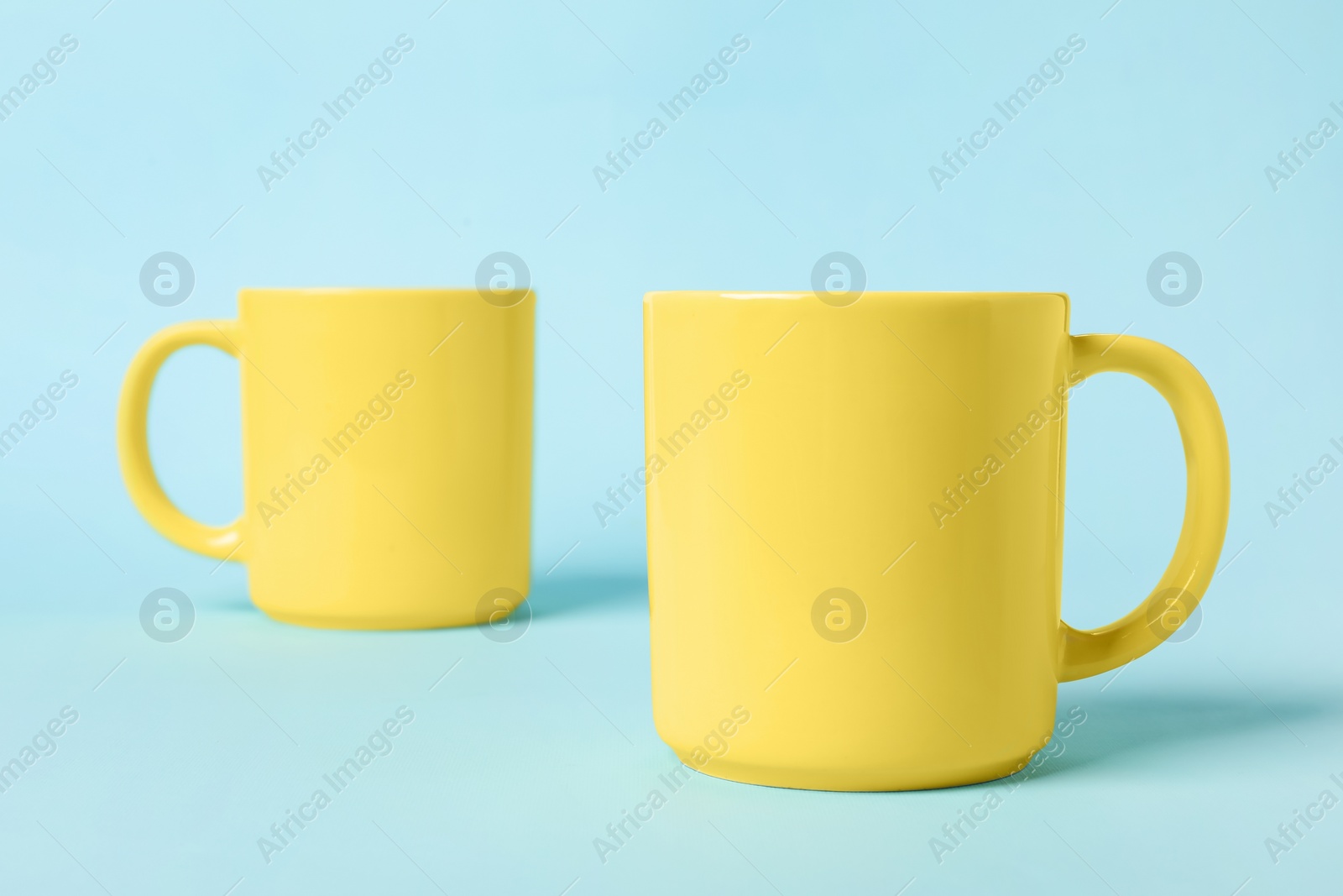 Photo of Two yellow ceramic mugs on light blue background