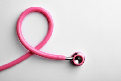 Photo of Pink stethoscope folded like awareness ribbon on white background, top view with space for text. Breast cancer concept