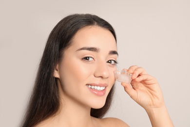 Photo of Young woman with ice cube on light background. Skin care