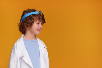 Photo of Little boy in medical uniform with head mirror on yellow background. Space for text
