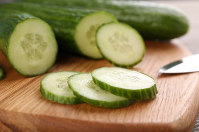 Photo of Cucumbers and knife on wooden cutting board, closeup