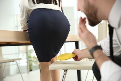 Photo of Young man putting whoopee cushion on chair while his colleague sitting down in office, closeup. Funny joke