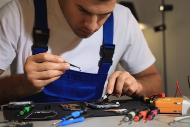 Photo of Technician repairing broken smartphone at table indoors, closeup