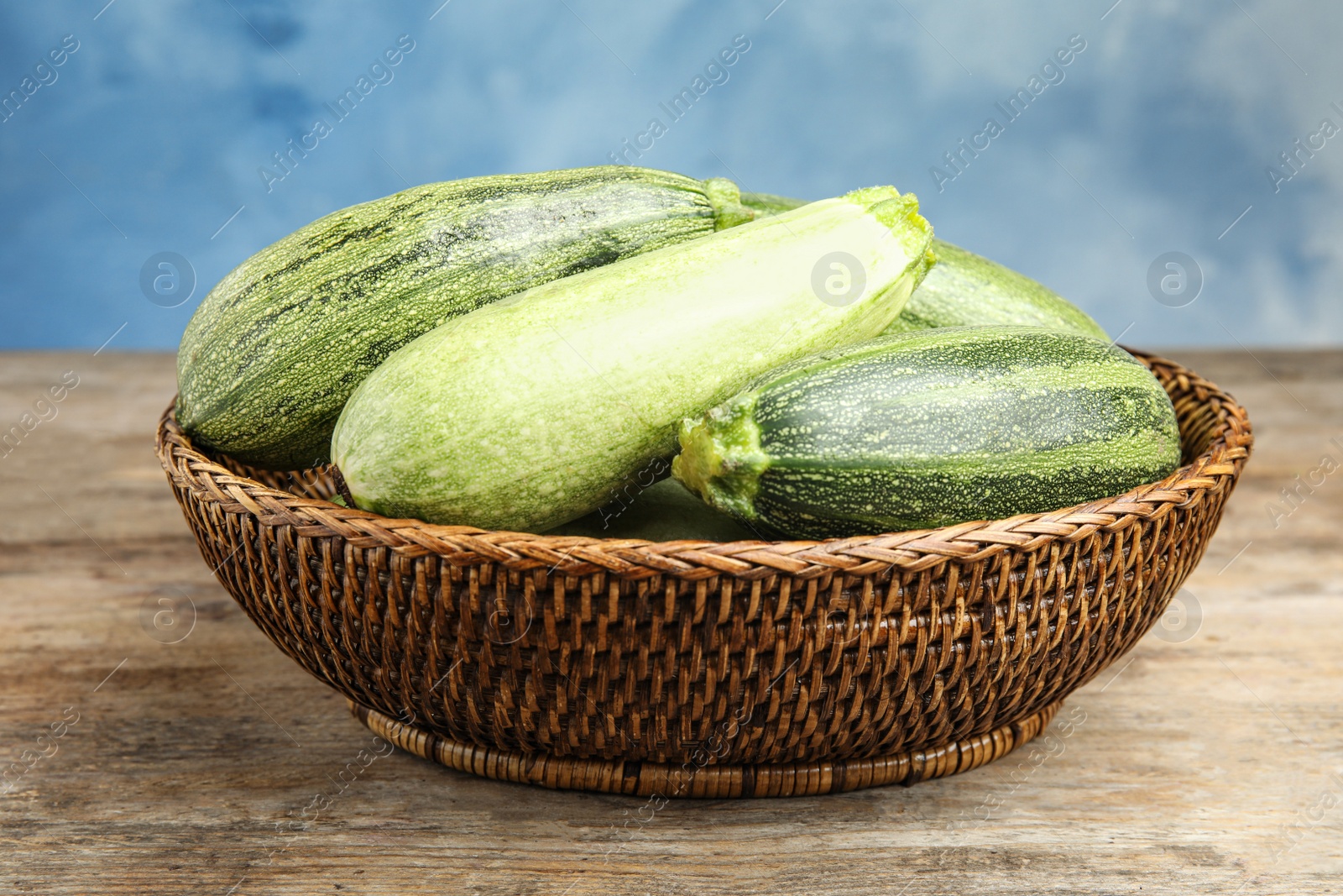 Photo of Wicker bowl with fresh ripe green zucchini on wooden table