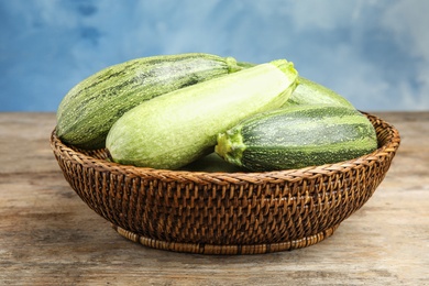 Photo of Wicker bowl with fresh ripe green zucchini on wooden table