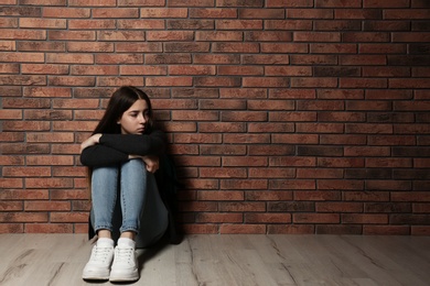 Photo of Upset teenage girl sitting on floor near wall. Space for text