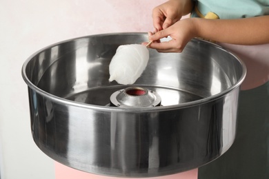 Photo of Young woman making cotton candy with modern machine on pink background, closeup