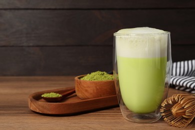 Photo of Glass of tasty matcha latte, bamboo whisk and green powder on wooden table, space for text
