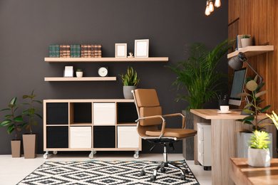 Photo of Comfortable workplace with computer near wooden wall in stylish room interior. Home office design