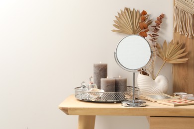 Photo of Makeup table with mirror, perfumes and burning candles in room. Space for text