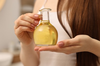 Photo of Natural hair mask. Woman holding jug of oil at home, closeup