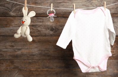 Photo of Bodysuit, pacifier and toy bunny on laundry line against wooden background. Baby accessories