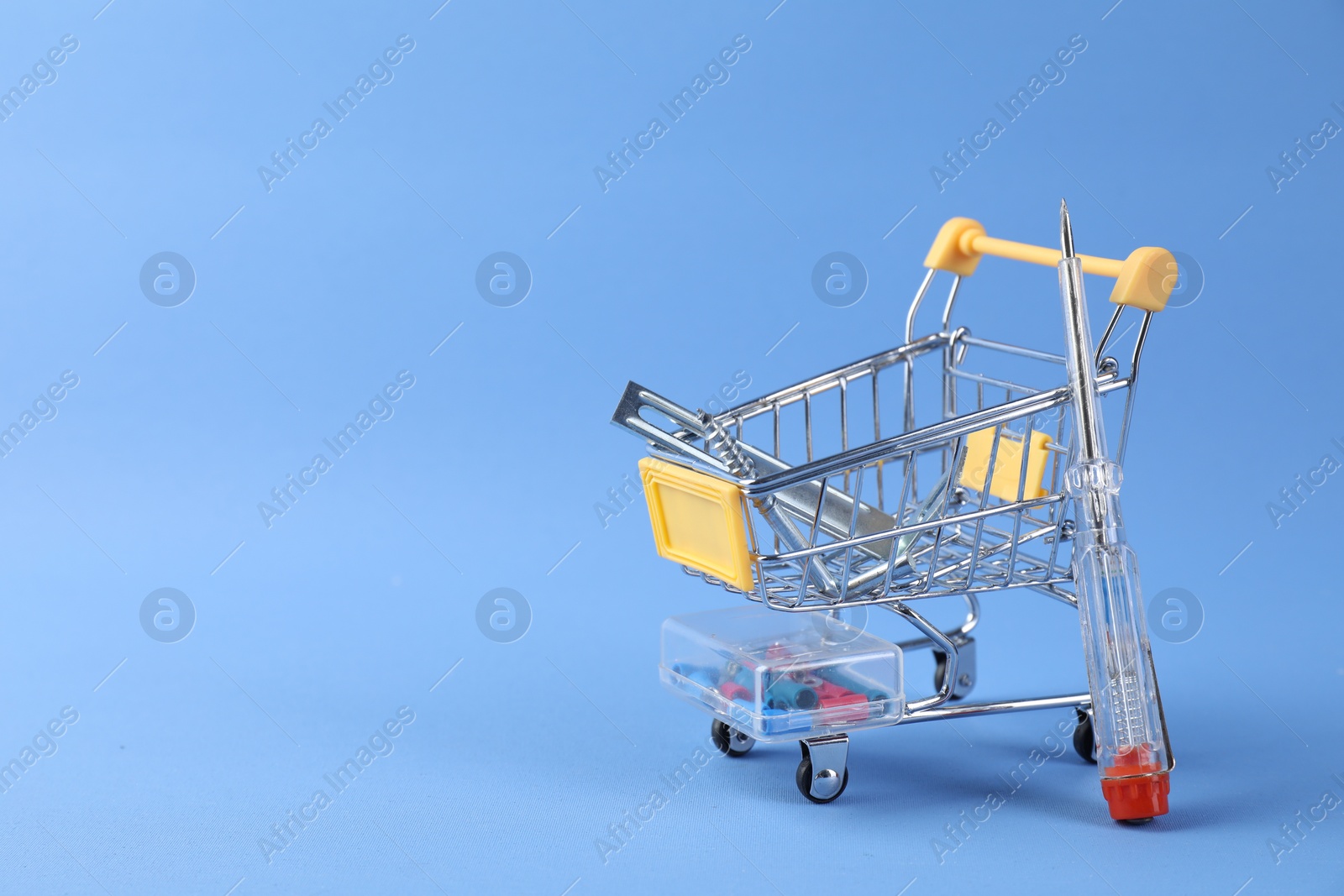 Photo of Small shopping cart with set of construction tools on light blue background. Space for text