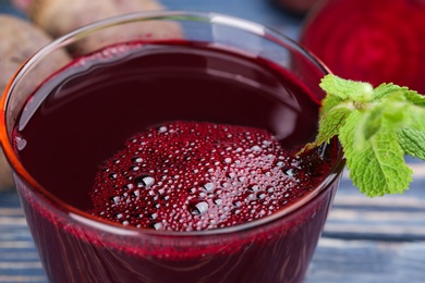 Photo of Freshly made beet juice in glass on blue table, closeup