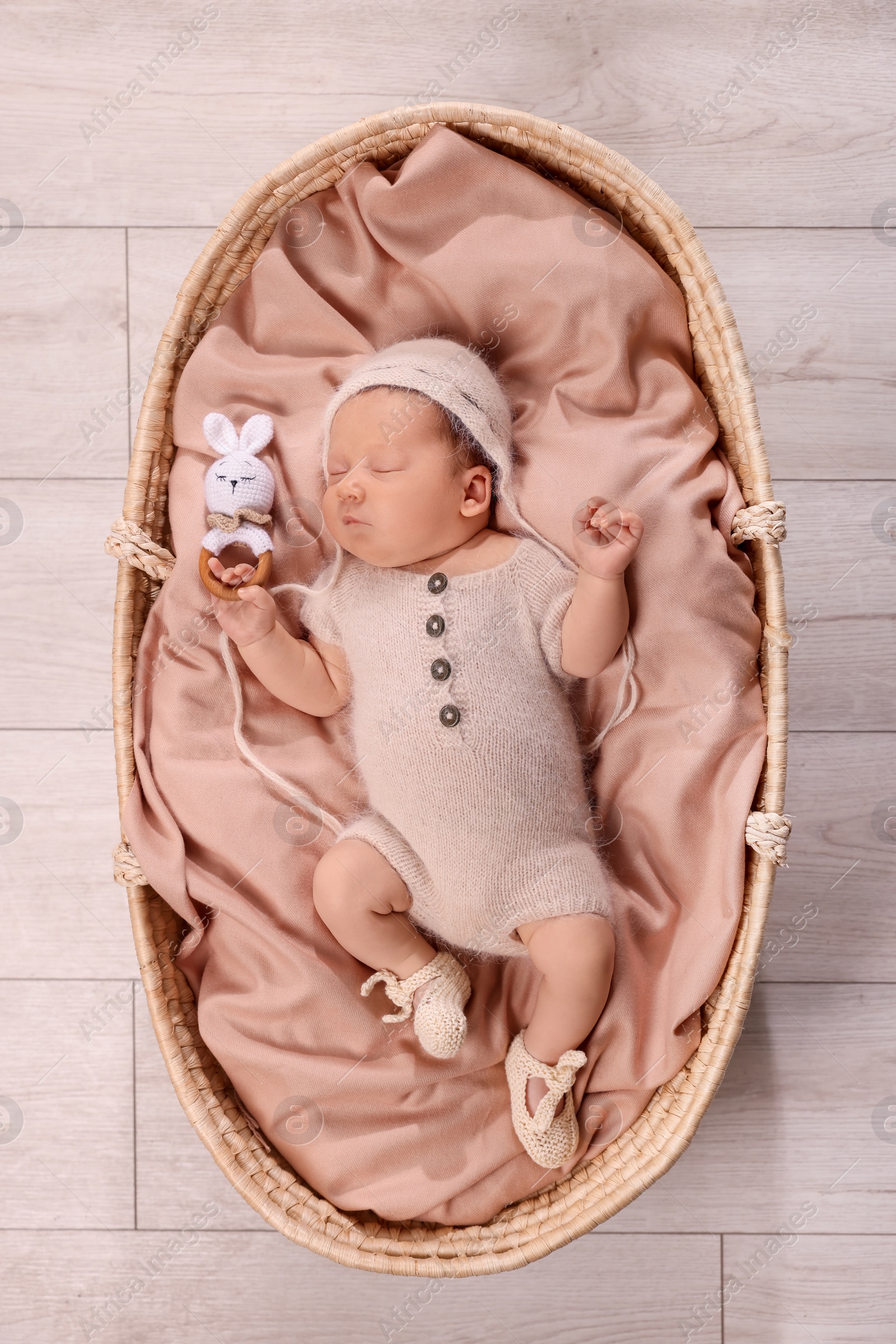 Photo of Cute newborn baby sleeping with rattle in wicker crib indoors, top view