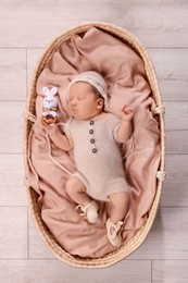 Photo of Cute newborn baby sleeping with rattle in wicker crib indoors, top view