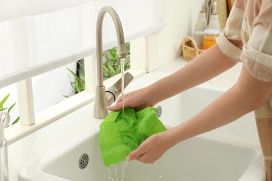 Photo of Woman washing beeswax food wrap under tap water in kitchen sink, closeup