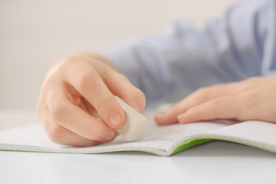 Photo of Boy erasing mistake in his notebook at white desk, closeup
