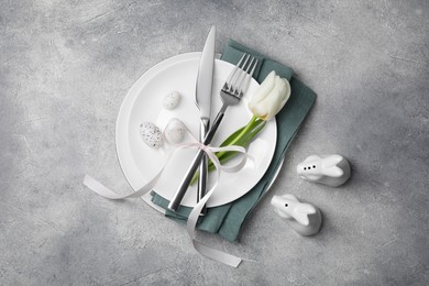 Photo of Festive table setting with painted eggs and white tulip on light grey background, flat lay. Easter celebration