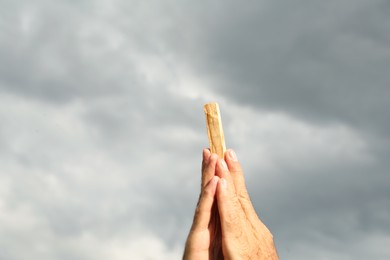 Photo of Man holding palo santo stick against gloomy sky, closeup. Space for text