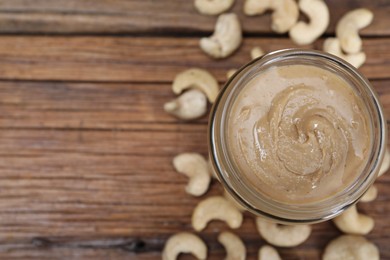 Tasty cashew nut paste in jar on wooden table, top view. Space for text