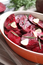 Photo of Baking dish with raw beetroot slices, garlic and rosemary on table, closeup