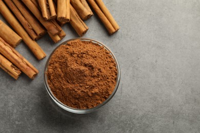 Photo of Bowl of cinnamon powder and sticks on grey table, flat lay. Space for text