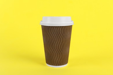 Photo of Brown paper cup with plastic lid on yellow background. Coffee to go