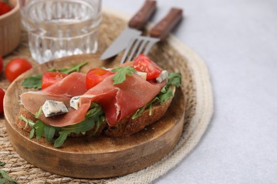 Photo of Tasty bruschetta with prosciutto, arugula, cheese and tomato served on light grey table, closeup
