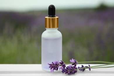 Photo of Bottle of essential oil and lavender flowers on white wooden table in field