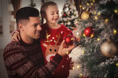 Photo of Happy father with his cute daughter decorating Christmas tree together at home