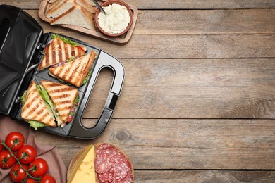 Modern grill maker with sandwiches and different products on wooden table, flat lay. Space for text