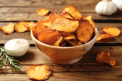 Photo of Delicious sweet potato chips in bowl, rosemary and sauce on table