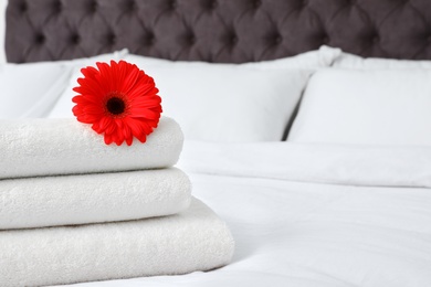 Photo of Stack of fresh towels with flower on bed indoors. Space for text