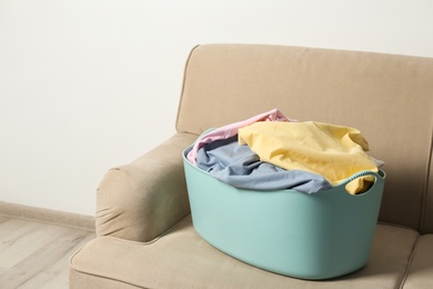 Photo of Laundry basket with dirty clothes on sofa indoors. Space for text