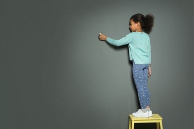 Photo of African-American child drawing with chalk on gray wall. Space for text