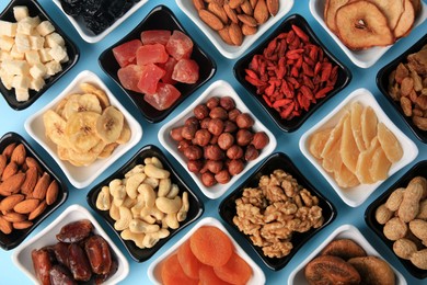 Photo of Bowls with dried fruits and nuts on light blue background, flat lay