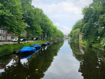 Photo of Beautiful view of city canal with moored boats surrounded by greenery