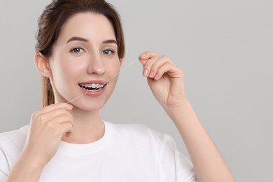Photo of Smiling woman with braces cleaning teeth using dental floss on grey background