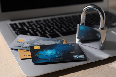Photo of Credit cards, lock and laptop on wooden table, closeup. Cyber crime
