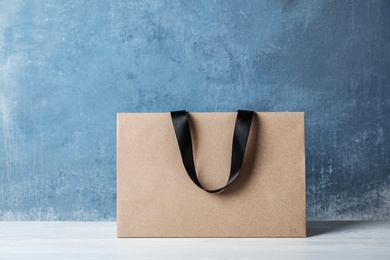 Paper shopping bag with handles on table against color wall. Mock up for design