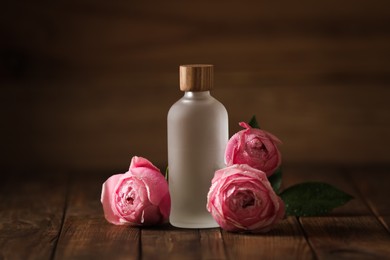 Bottle of essential rose oil and flowers on wooden table